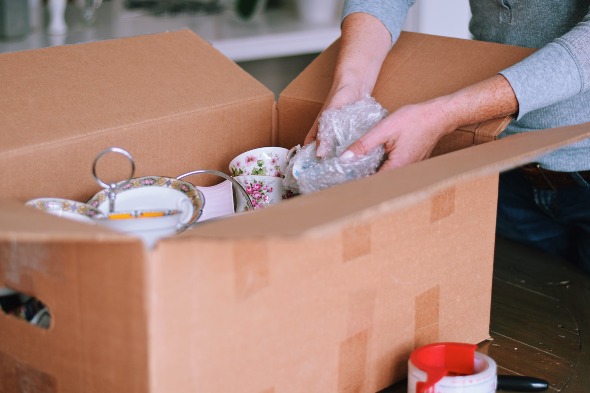 Woman packing fine china dishes into a cardboard box