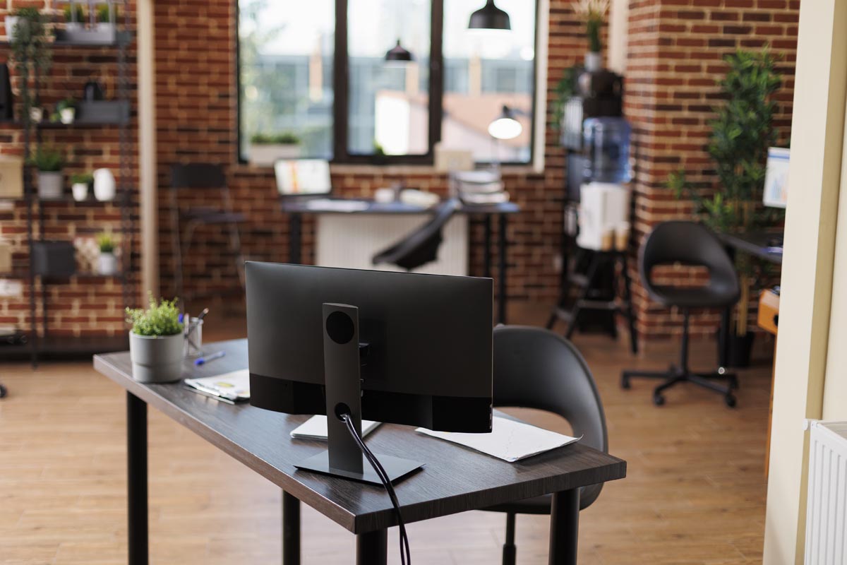 Interior of empty company office with furniture and nobody in it. Modern business marketing agency workspace with contemporary desks and desktop computers displaying financial charts.