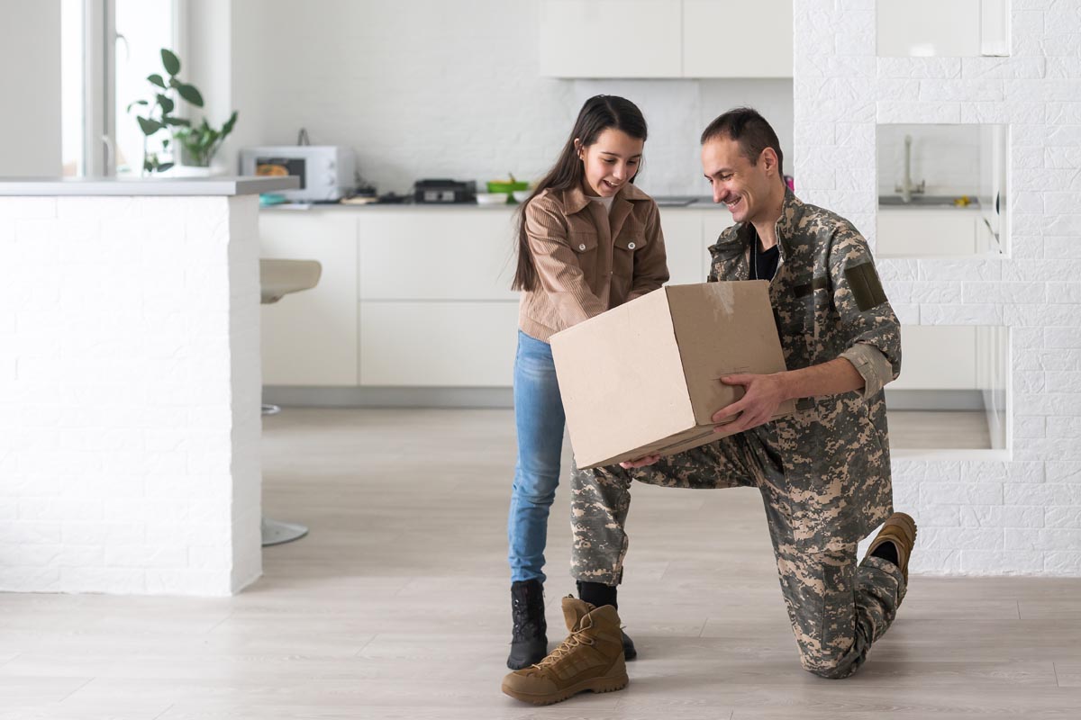 Military parents with daughter hugging, near cardboard boxes.