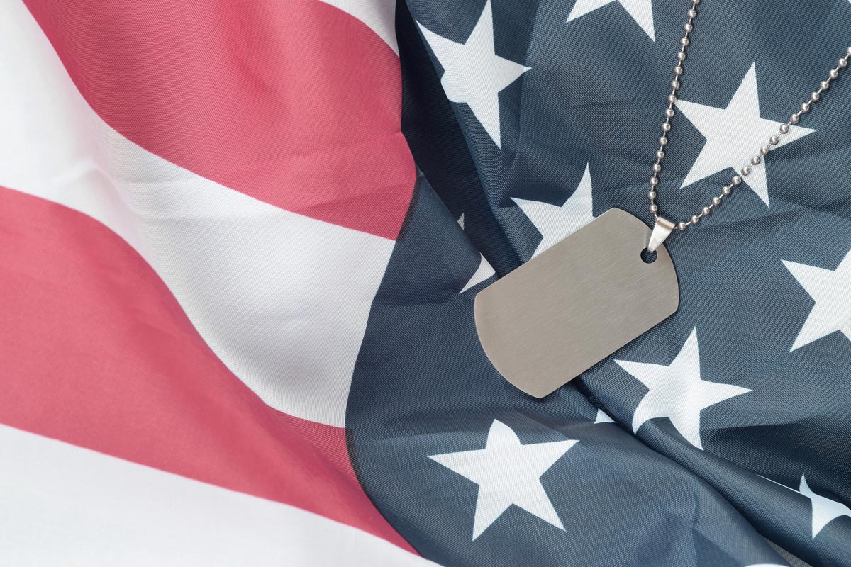 Silvery military beads with dog tag on United States fabric flag. Army token on USA banner close up. Veterans day concept