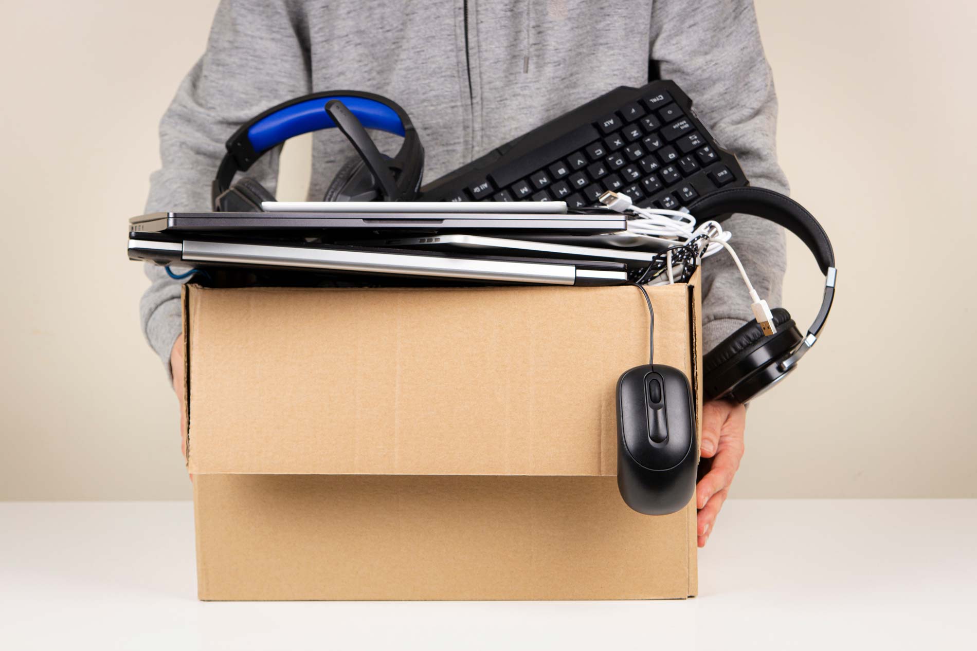 Man holding a box full of electronic devices including a keyboard and headphones