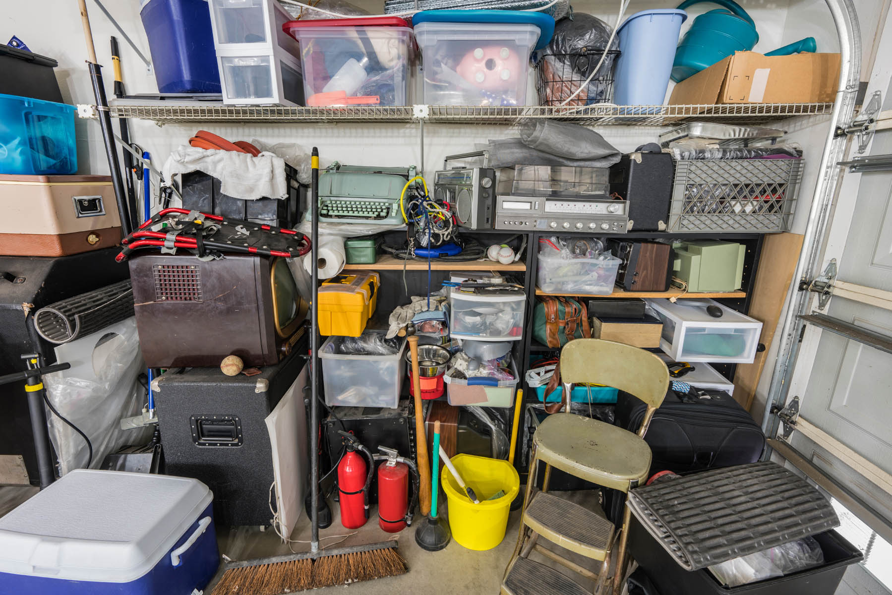 Messy cluttered junk filled suburban garage shelves with vintage electronics, houseware and sports equipment.